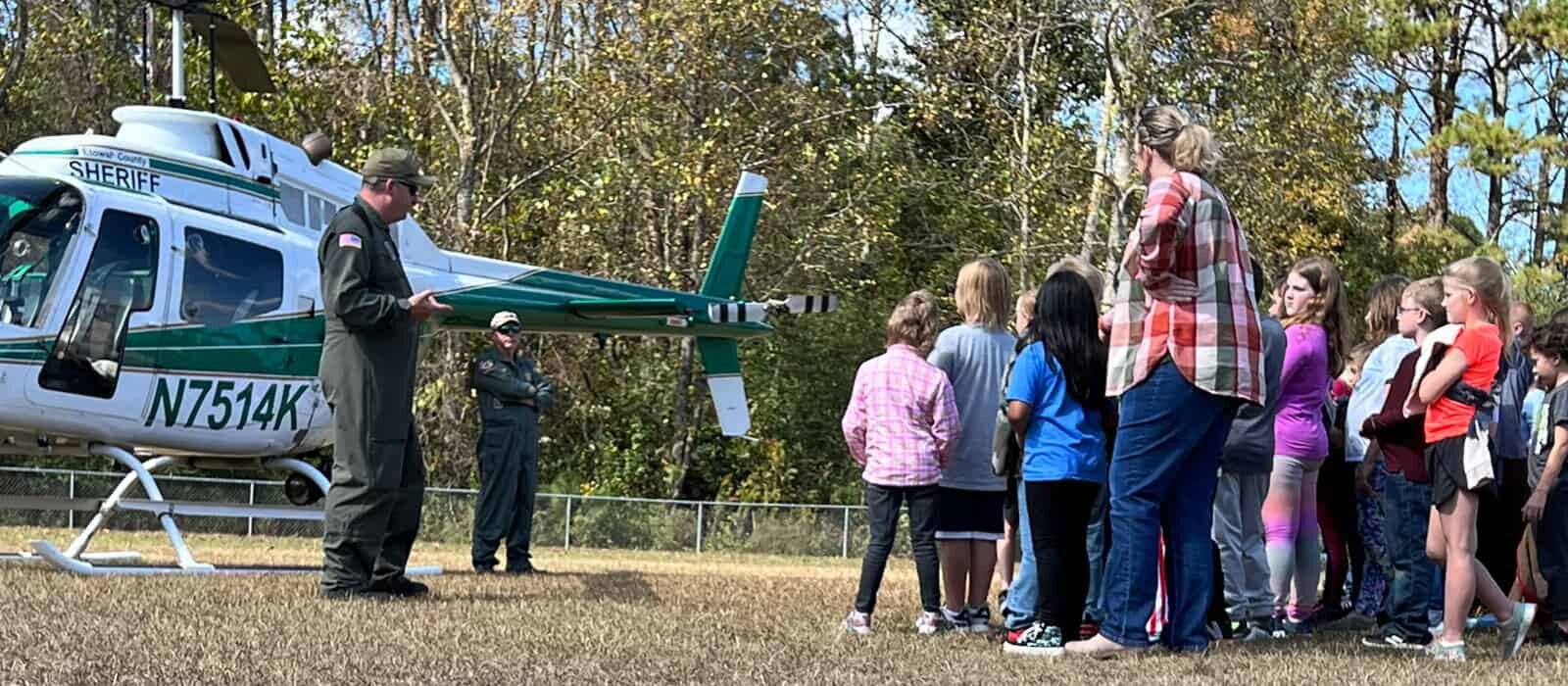 A group of young children being shown a Etowah County Sheriff's Office helicopter.
